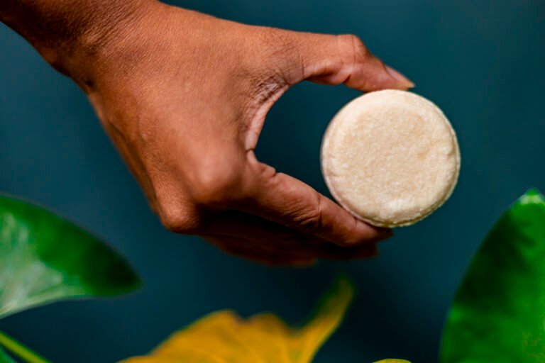 Como usar shampoo sólido e seus benefícios, mão segurando shampoo em barra com plantas ao redor